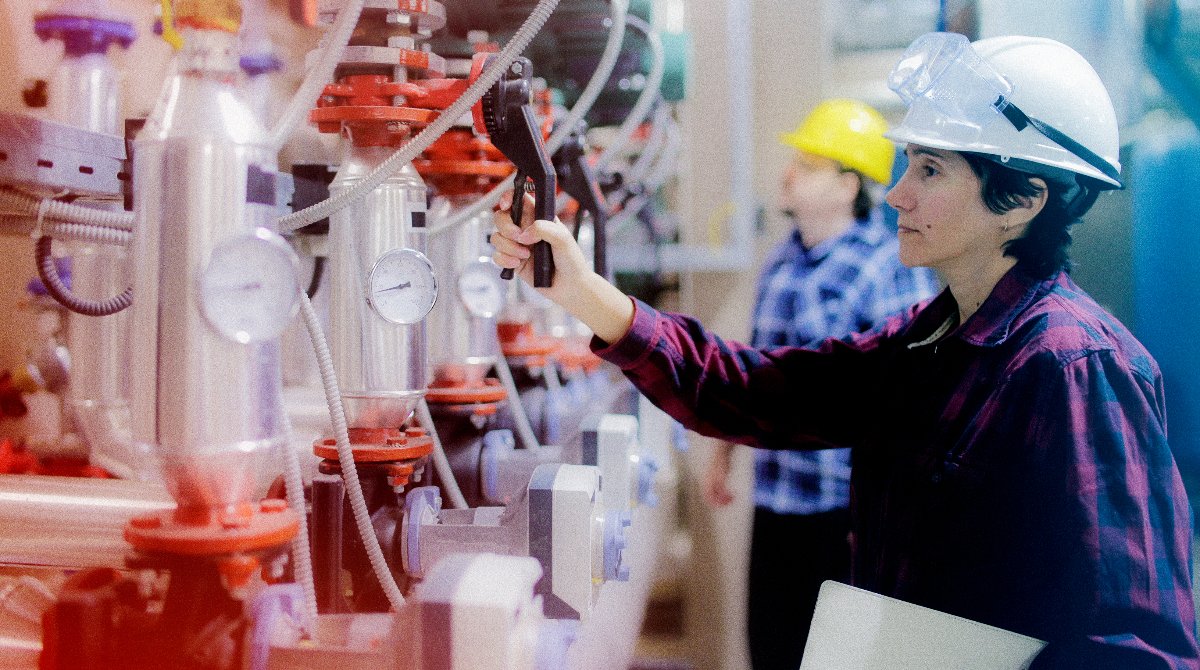 A female scientist adjusts a setting on a chemical container, in a laboratory, wearing a protective helmet and safety goggles.