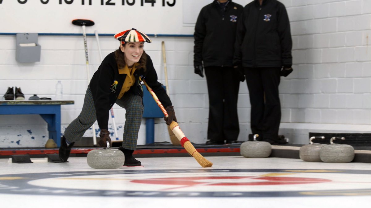 A woman is playing the sport curling. She is using equipment from the 1970s.