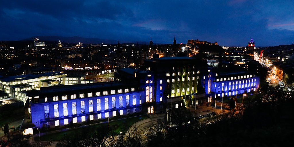 A photo of the exterior of the St Andrew's House building in Edinburgh, lit up in blue and yellow to represent the colours of the European Union flag.