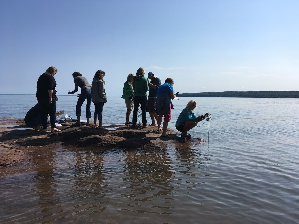 Teachers stand on the edge of the water and collect water samples from the bay.