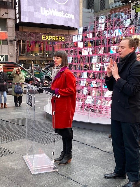 Andrea speaks at a podium in front of the Heart Squared