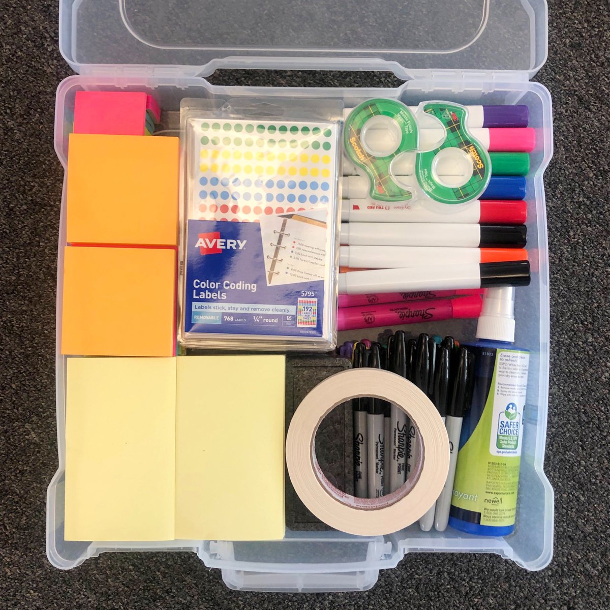 A clear plastic case containing neatly organized post-it notes, sharpies, stickers, tape, scissors, and whiteboard markers.