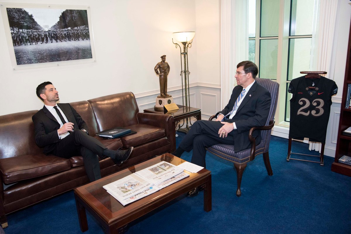 Secretary Esper, seated in a chair, talks with DHS Acting Secretary Chad Wolf, who is seated to the left on a couch.
