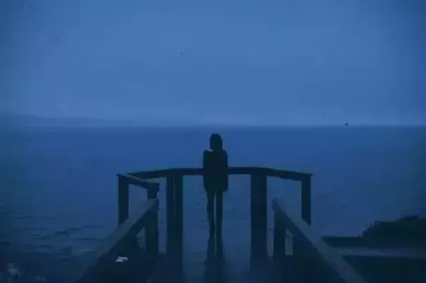 Lone woman stares out across a blue, misty sea. It's a rather gloomy image. She looks very isolated.