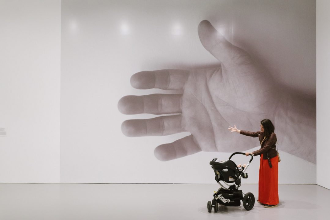 A figure with a stroller stand in front of an art installation with a graphic of a hand