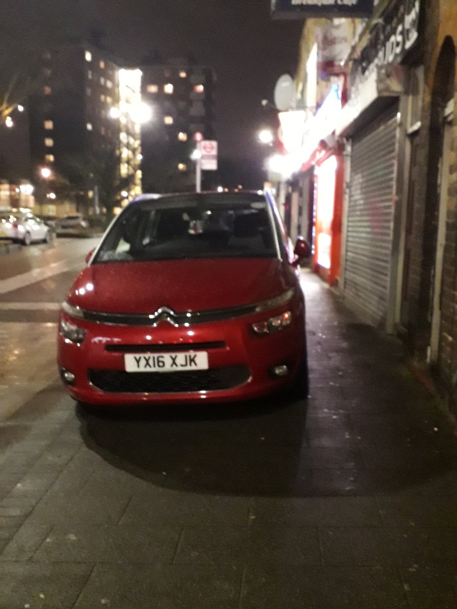 A car parked on pa pavement in front of shops leaves a narrow gap for pedestrians to get through 