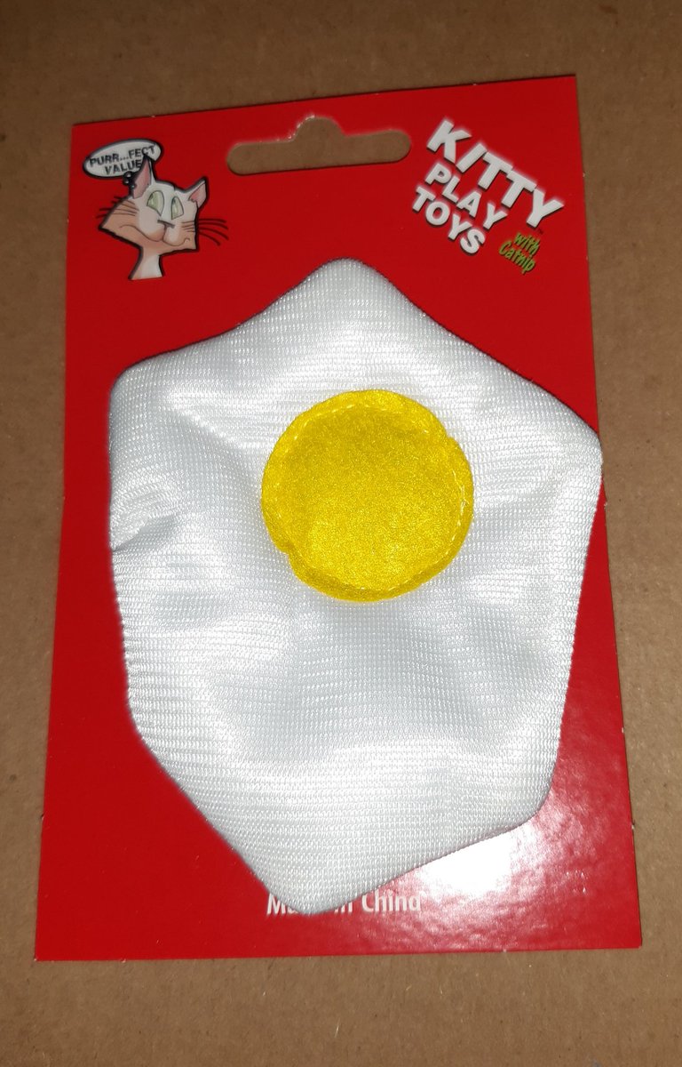 A picture of a toy fried egg attached to a red cardboard backing with a picture of a cat and a speech bubble reading "purr... fect value" in the upper left corner and the text "Kitty Play Toys with Catnip" in the upper right corner.