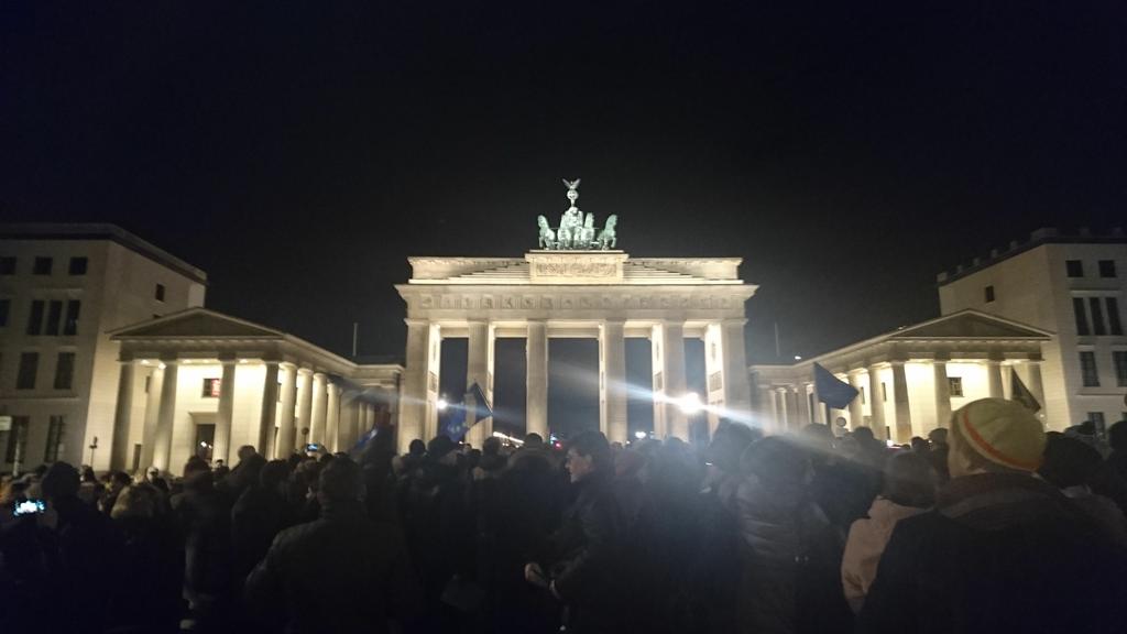 Brandenburger Tor at night with a crowd of people holding up EU flags and signs saying "Je suis Européenne".