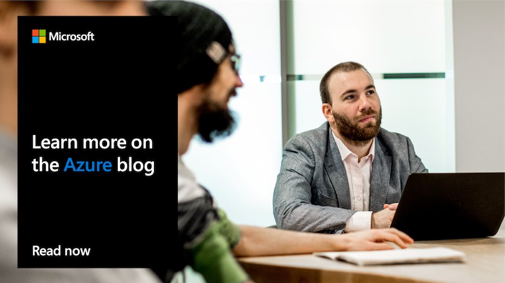 Photo of men sitting at a table, one in a gray suit looking up.