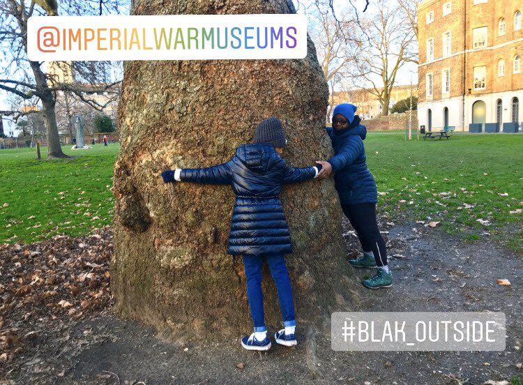 Females holding hands hugging a large tree