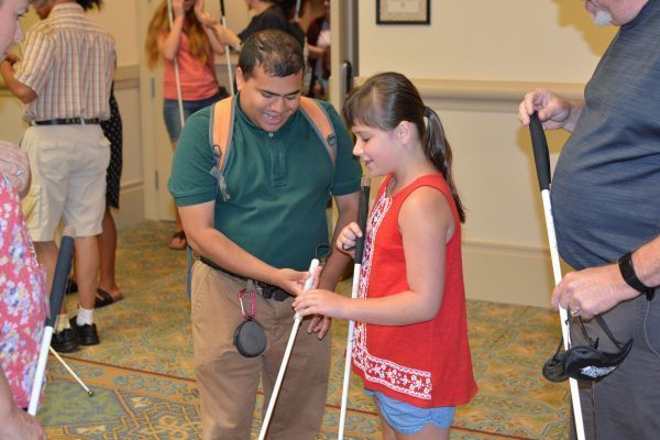 A young girl looks at a long white cane from the free white cane program