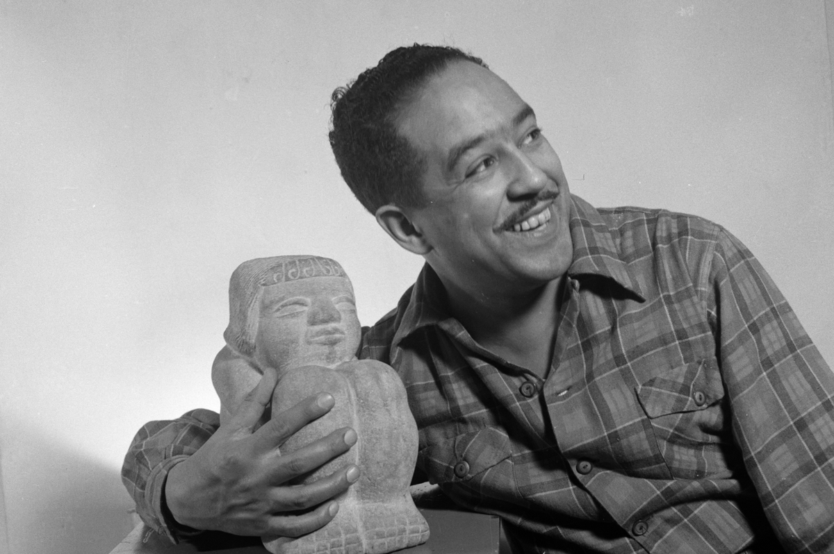 Photo of Langston Hughes smiling and looking to the right (his left). Hughes was born on this day in 1902.