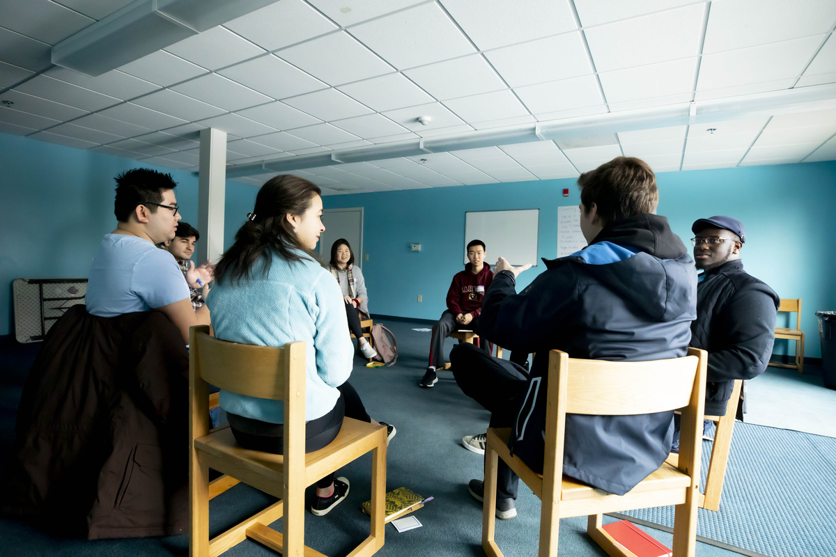 Students sit in a circle of wooden chairs
