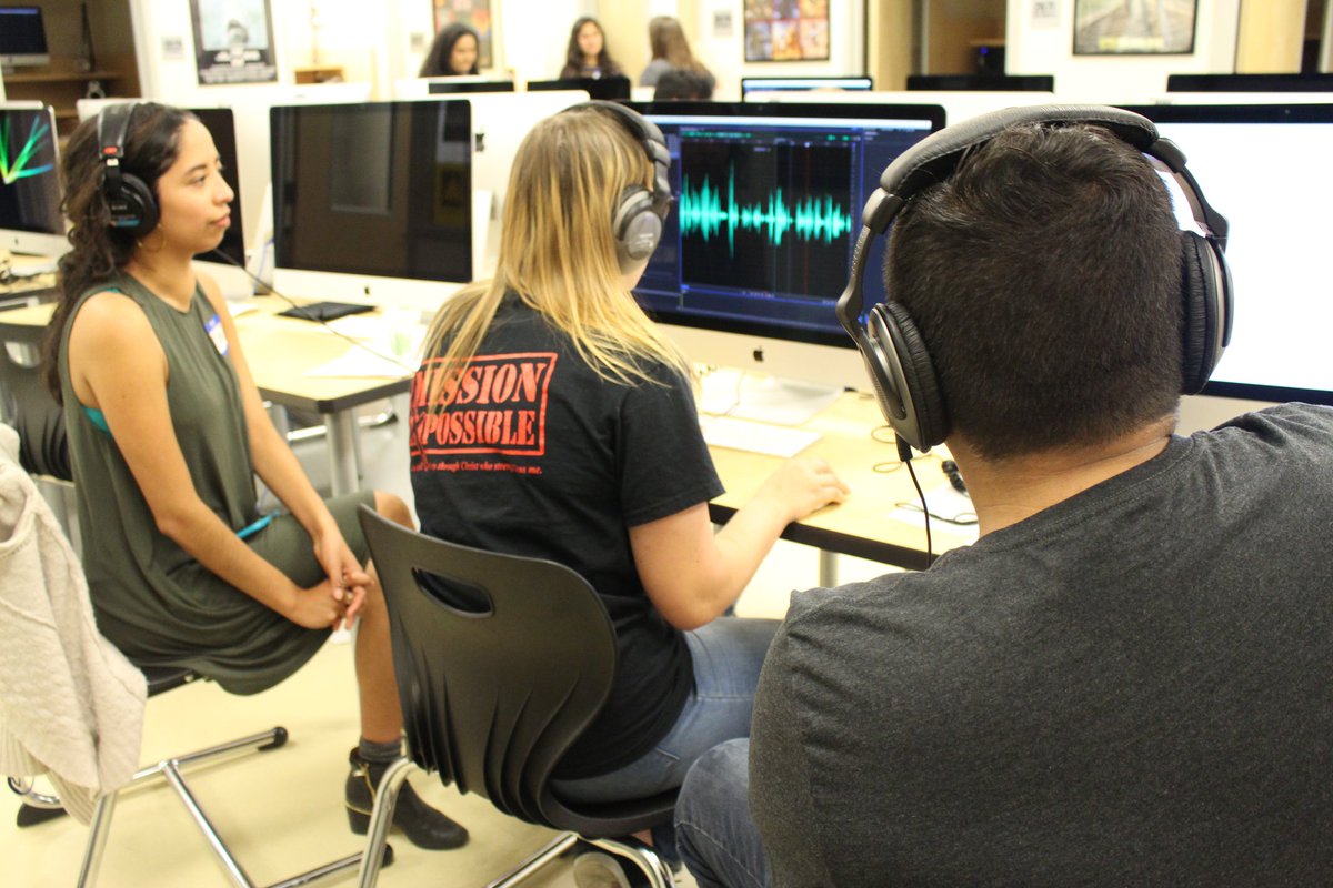 Photo: Two students and a mentor, all wearing headphones, look at a computer screen where they are editing audio using Adobe Audition software.