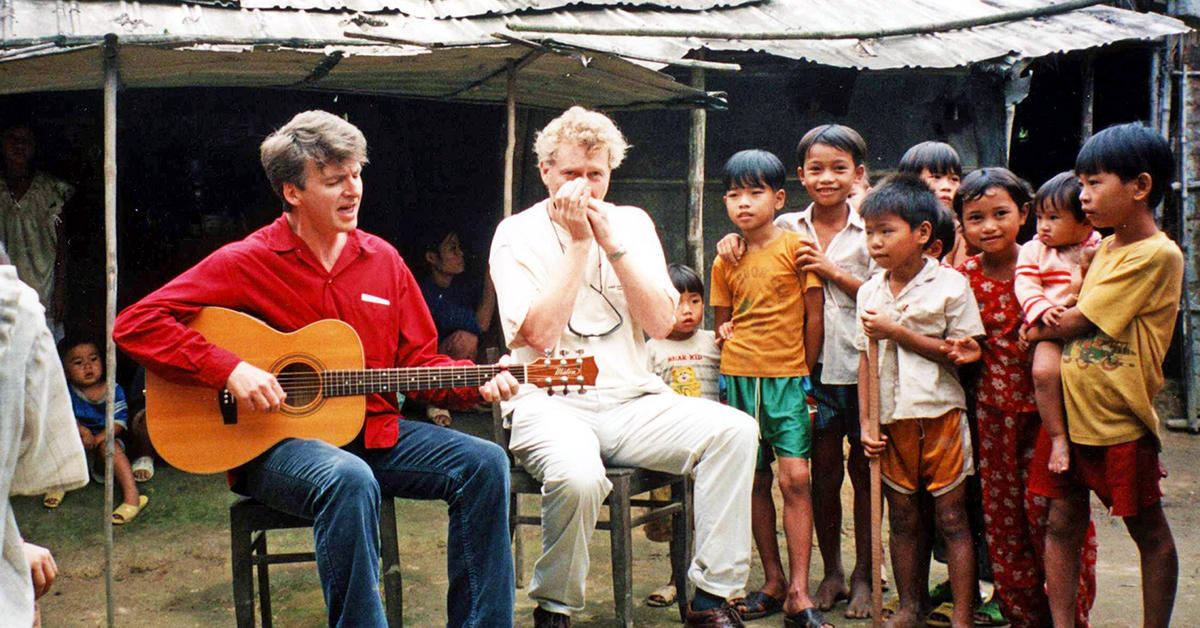 Neil Finn playing guitar in a village in Vietnam in 1998.