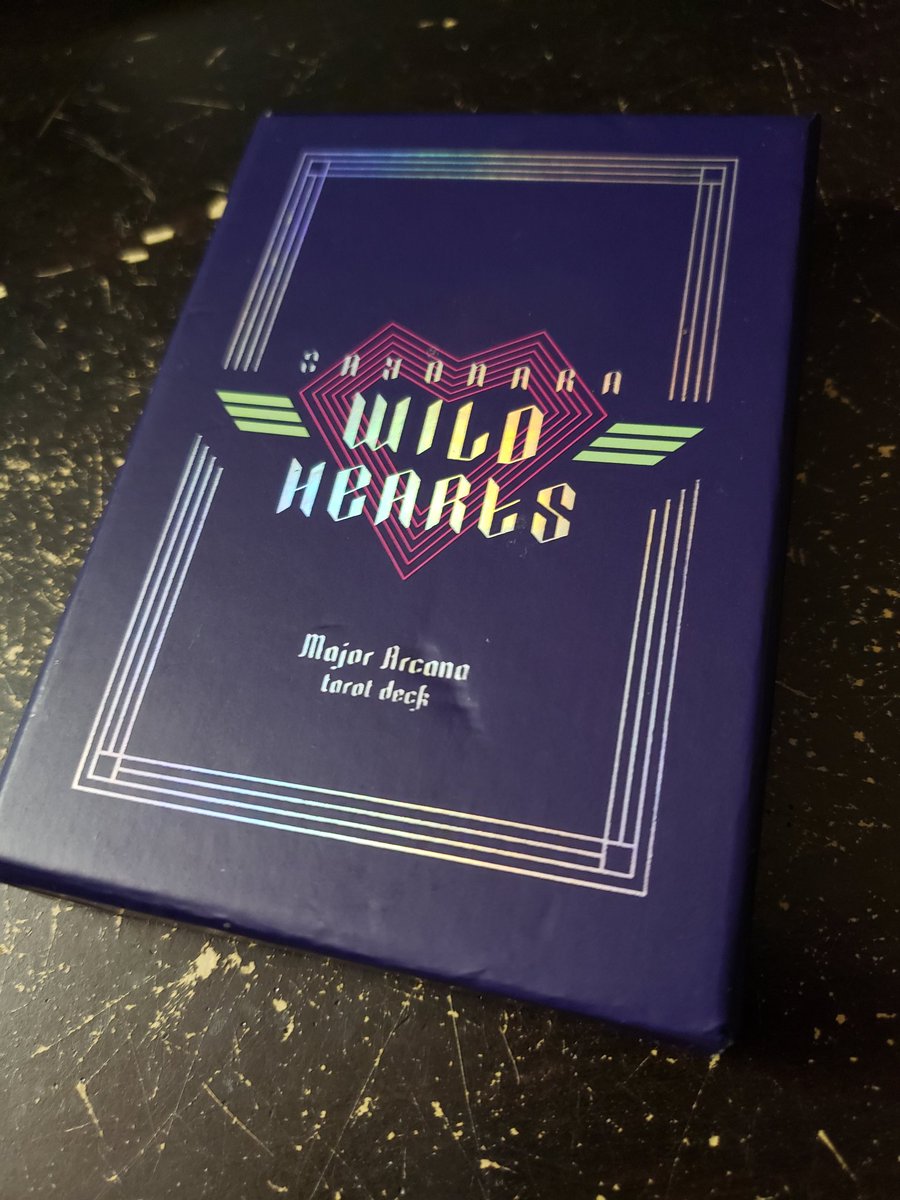 A closeup of the aforementioned box of tarot cards. It features the logo of the came on the center of the box, and reads "Major Arcana tarot deck" underneath, all surrounded by a rectangular border. The text and lines are a silver, holographic material.