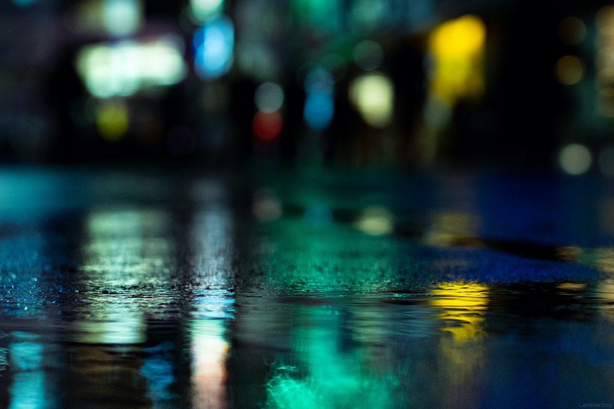 Photography of Tokyo at night by Liam Wong. An out of focus bokeh image focused on the ground in front as silhouettes pass by. It is green and yellow in color.
