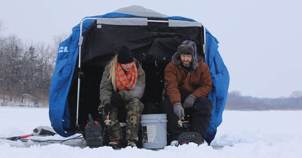 woman and man ice fishing in a portable ice shelter on a cloudy day