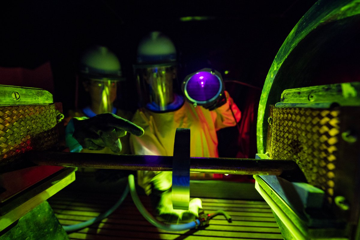 Two Airmen in full body protective suits carry out a scientific test in a dark laboratory.