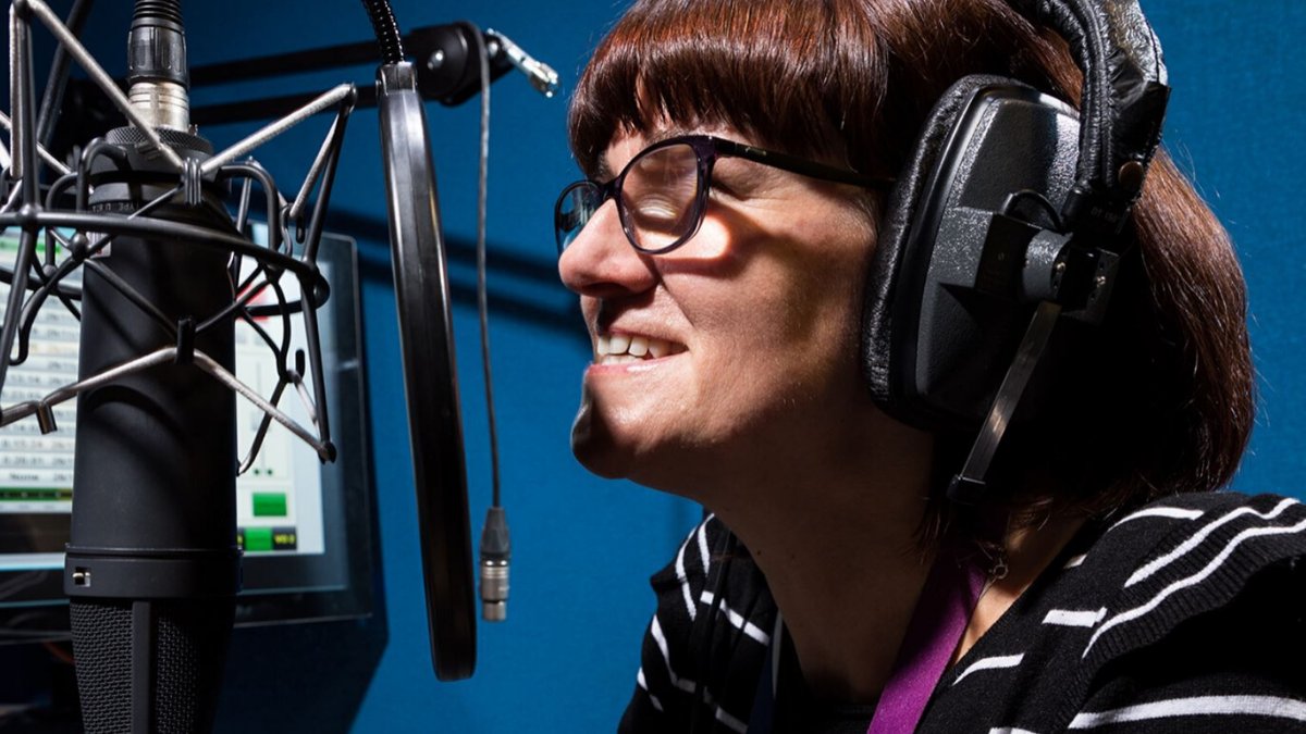 Woman wearing headphones and talking to a microphone.