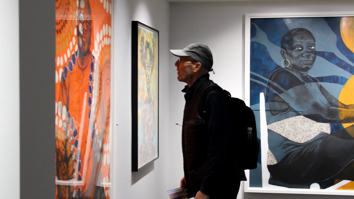 A man looks closely at the large, colorful, patterned portraits in "Delita Martin: Calling Down the Spirits."