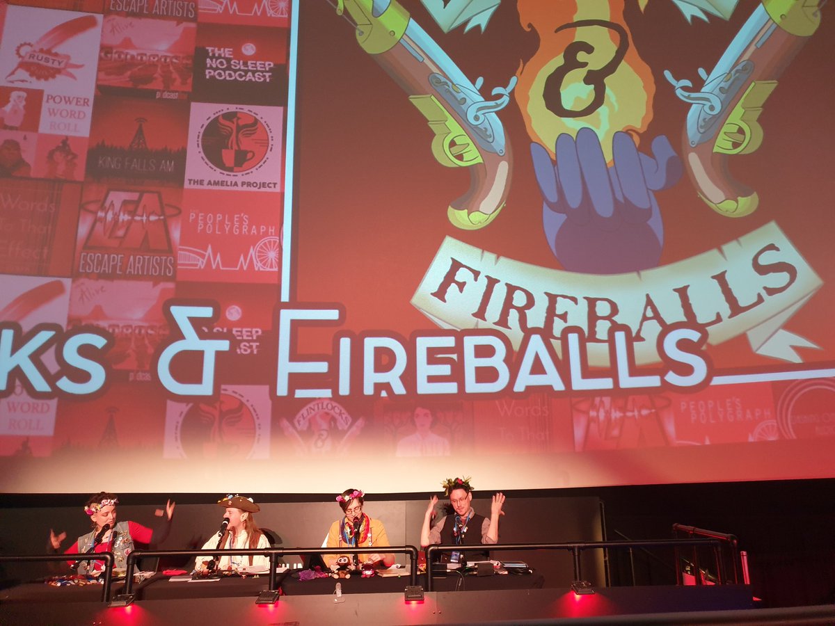 Ellie, Sam Robbie and Jason sat at a table with microphones during the live show with an enormous flintlocks and fireballs logo projected behind them