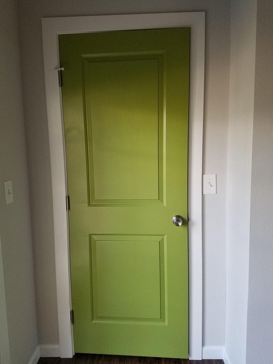 Bright green door surrounded by white trim against a very light gray wall.