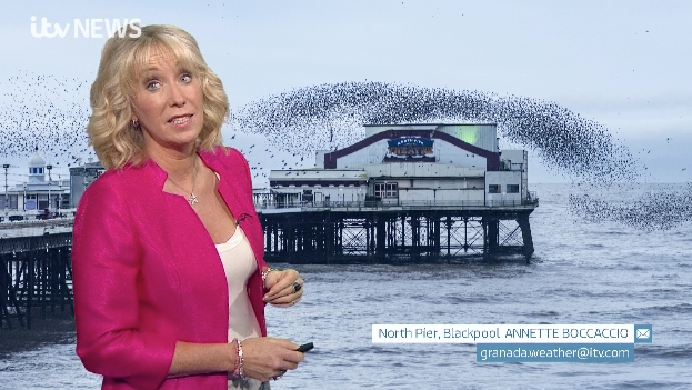 Emma in front of viewer's photo of Blackpool North Pier with a large shadow over it in the shape of a bird. It's actually a murmuration of starlings taken on Saturday