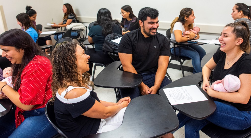 Students sit at desks in a classroom learning with baby dolls.