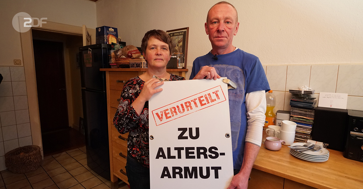 "ZDF.reportage: Wutsache - Abstiegsangst": Maren und Olaf Könemann stehen in ihrer Küche und halten ein Plakat mit der Aufschrift "Verurteilt zu Altersarmut" hoch.
