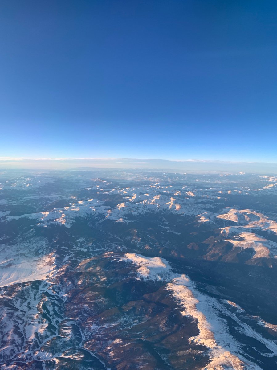 A view out my plane window: blue skies with a snow-capped mountain range below me, flying over Colorado.