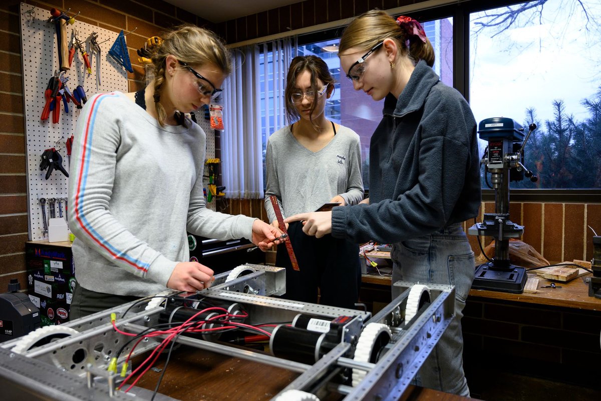 Three high school Women work tools on the base of a robot with wheels