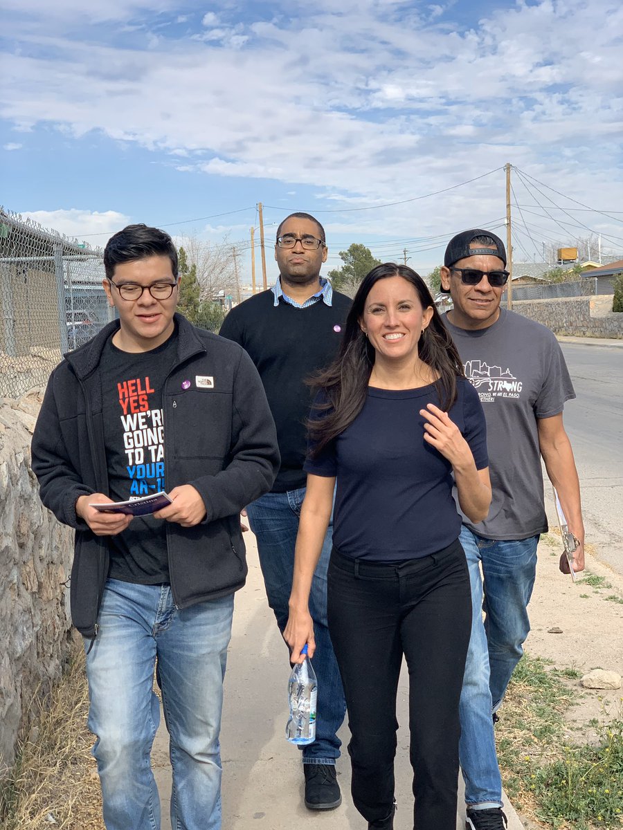 Cristina and three volunteers walk down the street with literature, a clipboard, and a water bottle in hand while block walking.