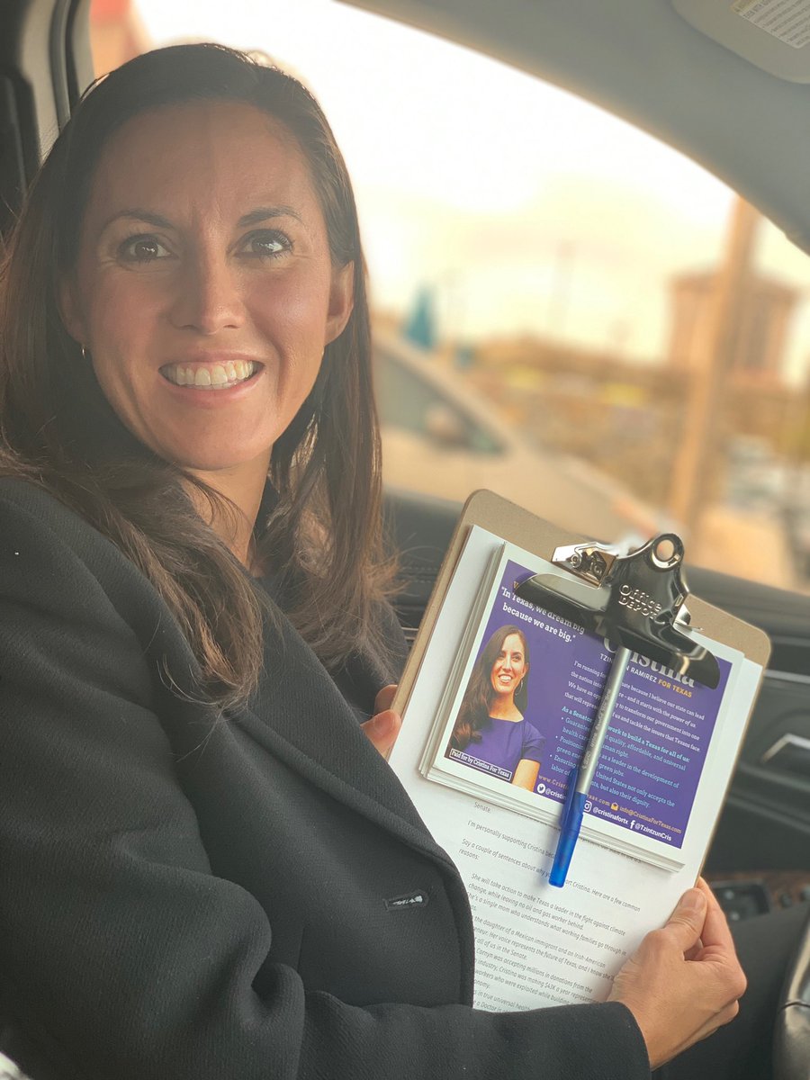 Cristina is smiling in a parked car, holding a clipboard with a pen and literature used for canvassing.