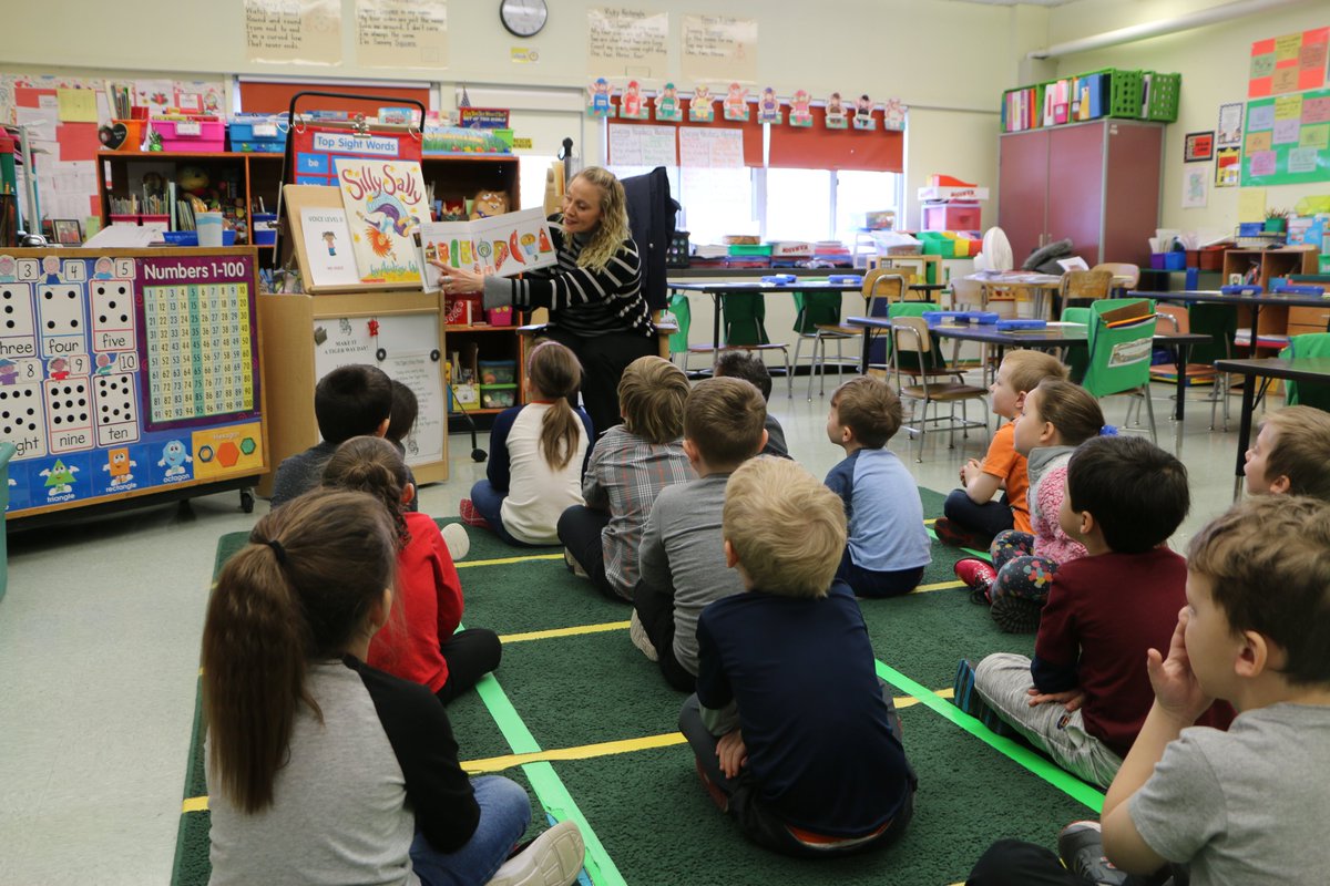 photo shows kindergarten students listening to a story being read aloud.