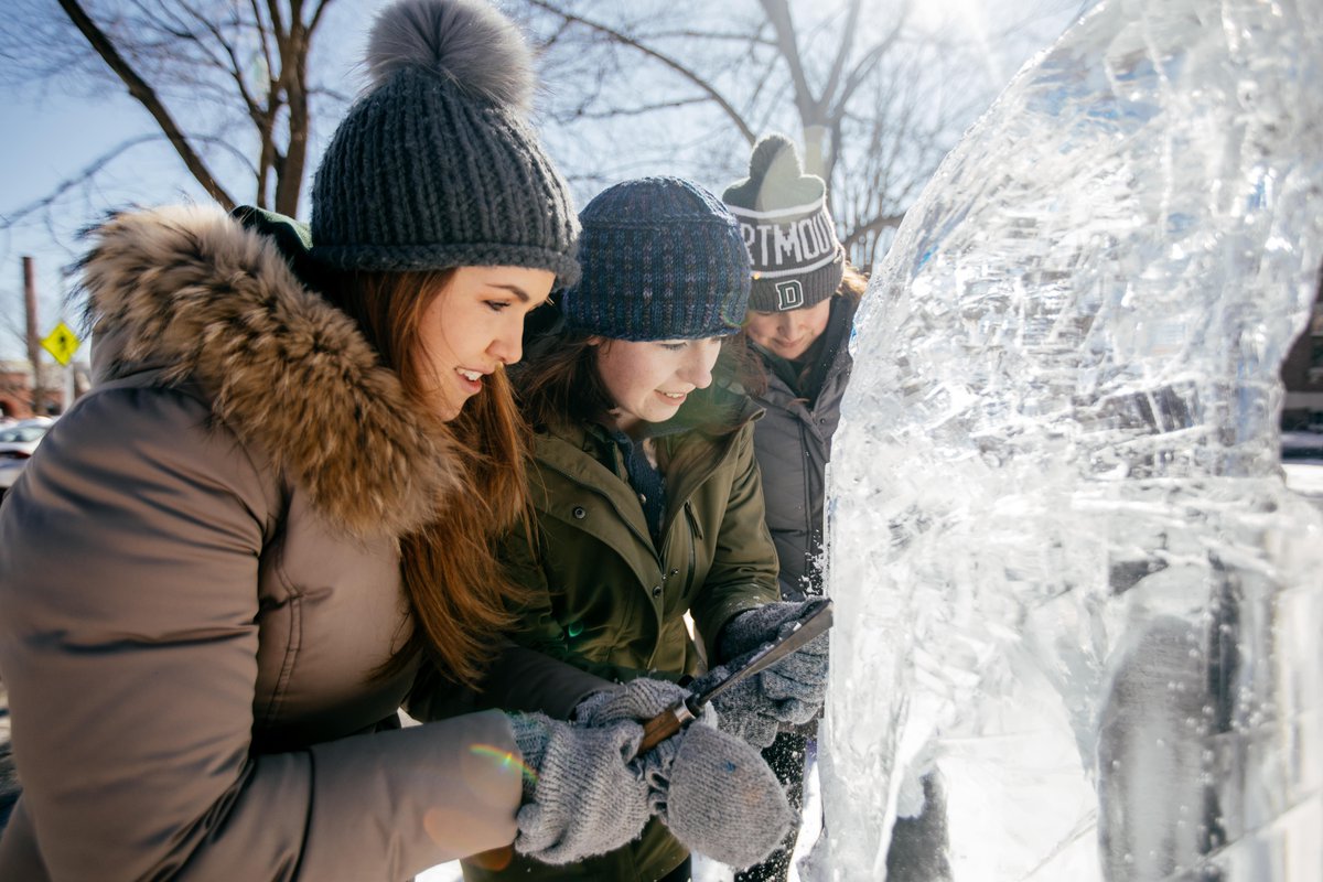 Three students bundled up in coats and hats carve an ice sculpture.