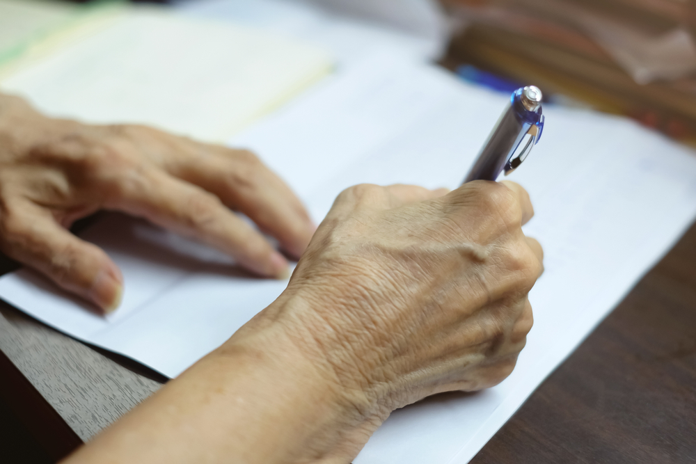 Elderly person with limited dexterity trying to fill in information using pen.