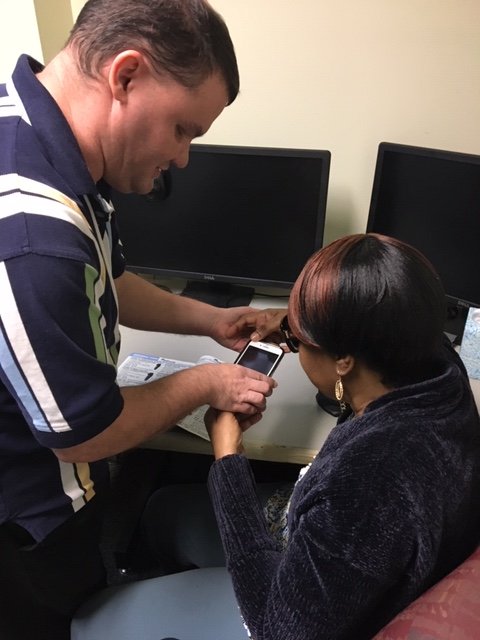 AT instructor, Casey M. works with an adult client to use a smartphone app that reads texts when scanned by the phone's camera.