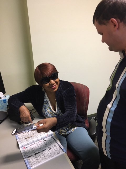 AT instructor, Casey M. works with an adult client to use a smartphone app that reads texts when scanned by the phone's camera.