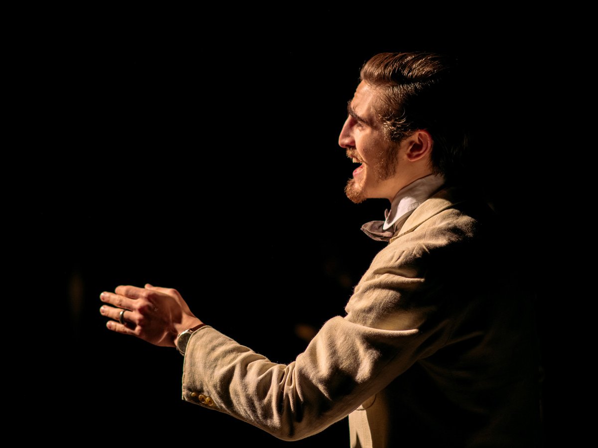 Actor in white linen suit gesturing in strong spotlight