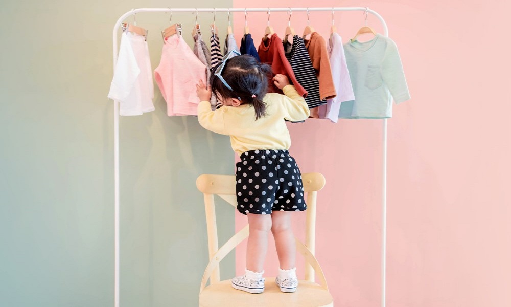 Girl stood on chair looking at a rail of clothes