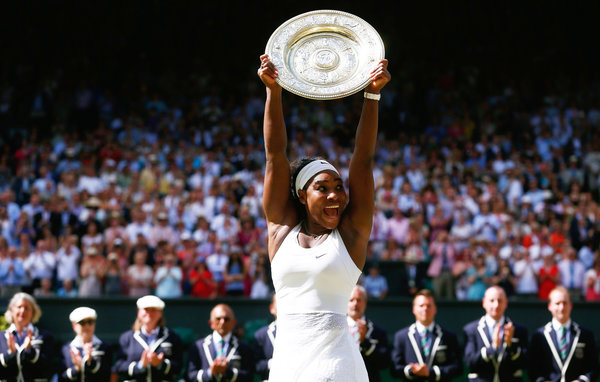 A photo of Serena Williams receiving her 2015 Wimbledon trophy on the court. She is raising it high in the air.