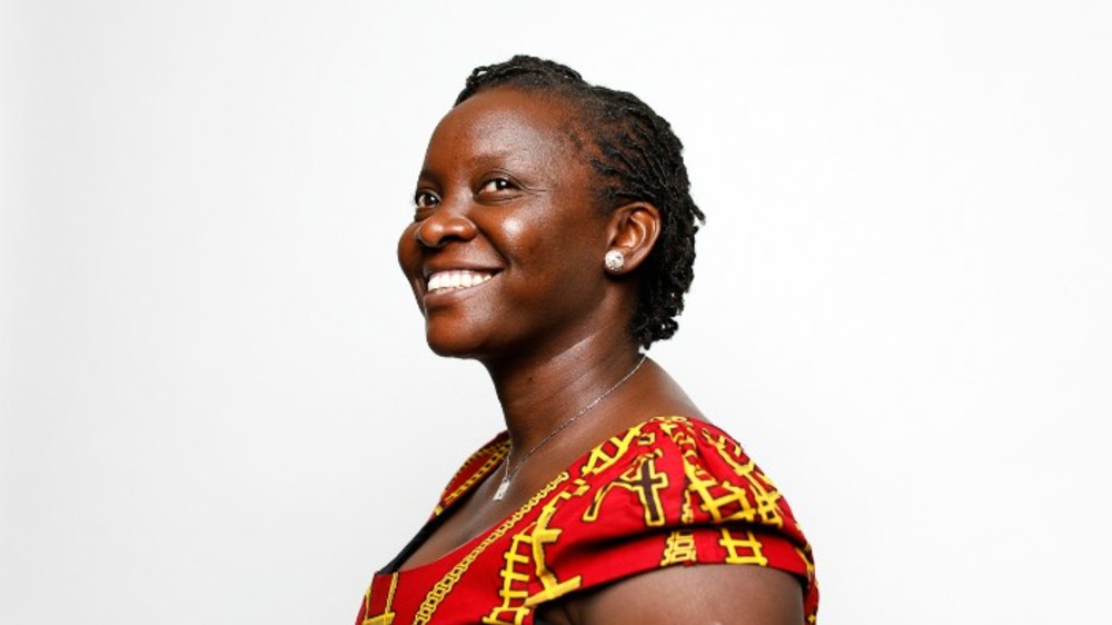 A woman wearing a red and yellow patterned shirt smiles as she looks off from the camera