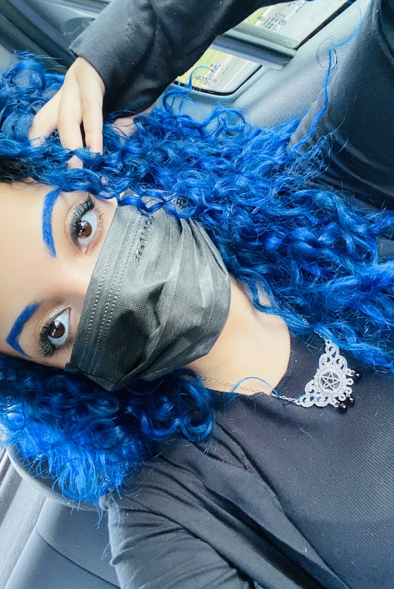 uma selfie minha, estou olhando diretamente pra câmera, vestida toda de preto e usando uma máscara de enfermeira também preta, usando um colar de pentagrama e tenho o cabelo e sobrancelhas azuis