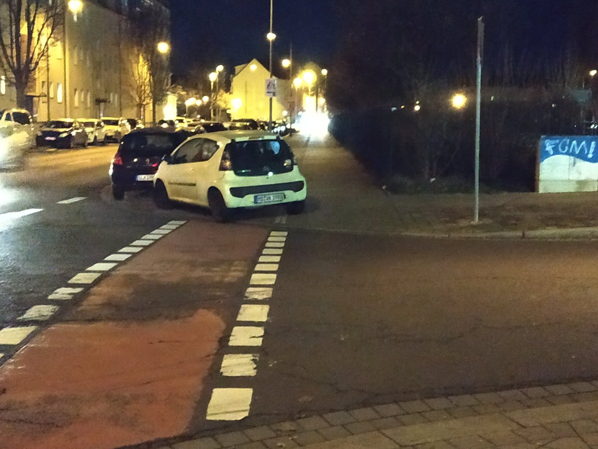 Ein Auto steht an einer Einmündung quer über der Auffahrt zum Fahrradweg