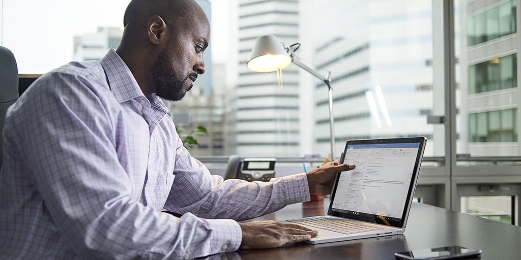 A man working on a Surface Book 2 by the window of an urban office. 