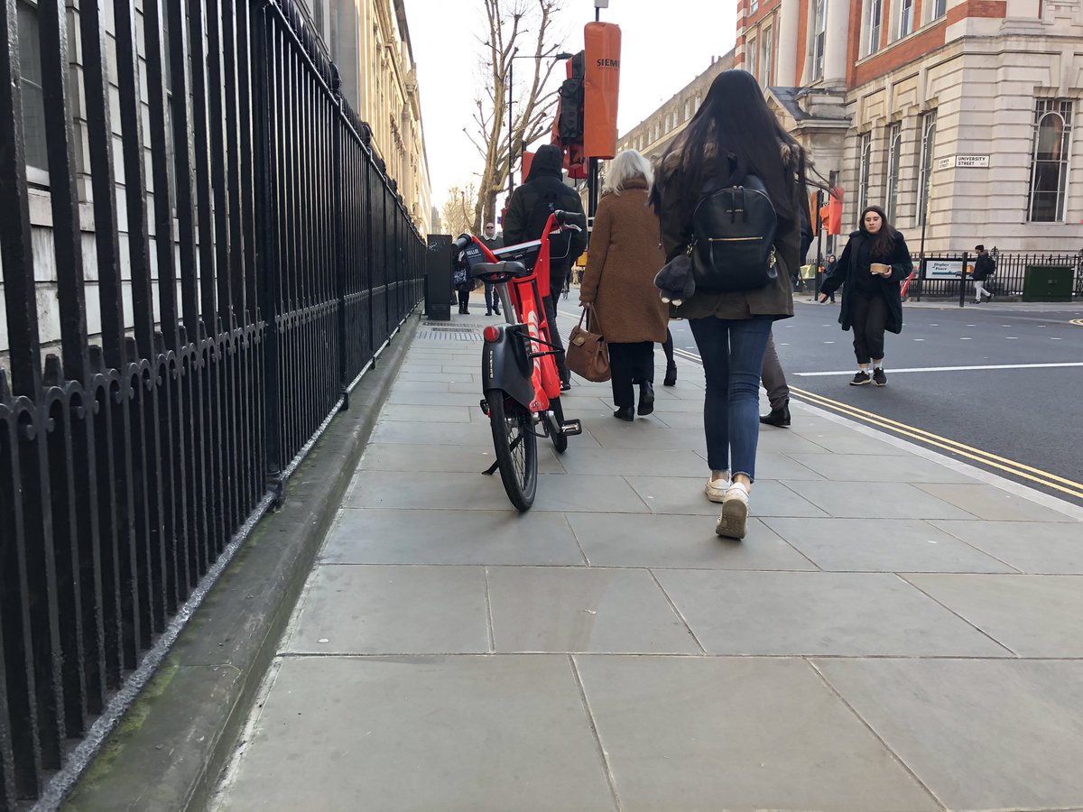 A red dockless bike parked in the middle of a narrow pavement