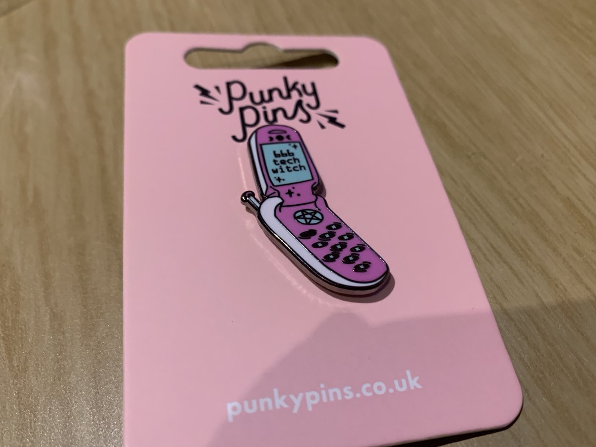 A pin that’s a pink flip phone that says 666 tech witch on the screen.