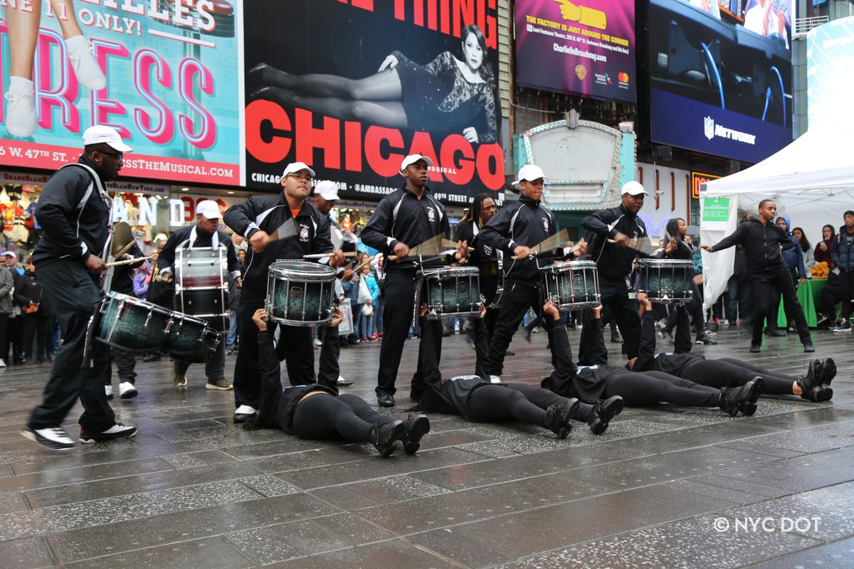 A group of people on a sidewalk dancing and playing music on drums. 
