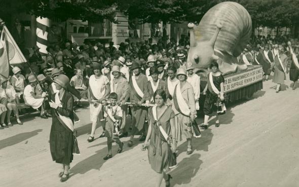 photo of suffrage campaigners pulling a giant paper mache snail through the street